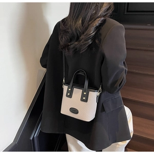 Sac seau beige tendance avec garniture en cuir noir porté par un mannequin dans un décor
