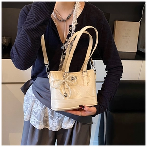 Detailed view of cream quilted handbag with pearl bow charm and silver hardware accents