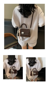 Detail of dark brown glossy crossbody bag with silver lock and decorative silk scarf accessory