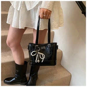 Detail of black quilted leather bucket bag with pearl bow charm and metal twist lock