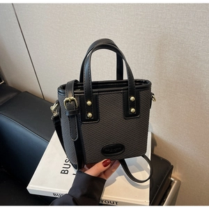 Vue détaillée du sac seau tissé gris avec anses en cuir noir et rivets dorés brillants