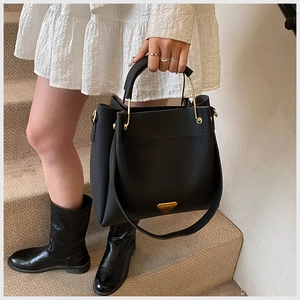 Detail of black lychee grain leather bucket bag featuring a gold triangular metal logo