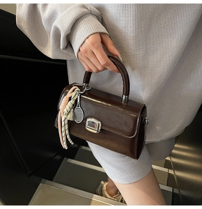 Detail of dark brown glossy handbag with metallic clasp and tennis racket charm