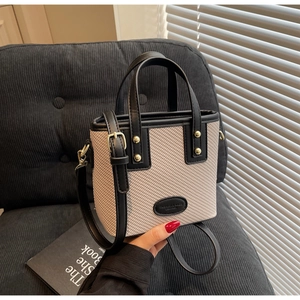 Détail du sac seau bicolore avec texture tissée, finitions cuir et clous dorés