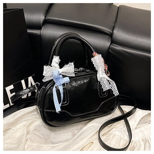 Detail of glossy black patent leather Boston bag with lace bow and blue plaid ribbon charm