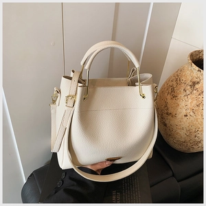 Detail view of lychee pattern leather handbag with triangular logo and adjustable strap