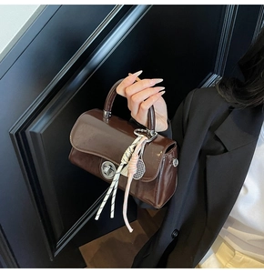 Détail d'un sac à main café brillant avec fermoir rotatif en métal et breloque de raquette