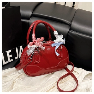 Detail of red patent leather Boston bag featuring decorative lace bowknots and handles