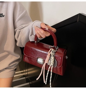 Close-up of wine red patent leather handbag with silver clasp and knot charms detail