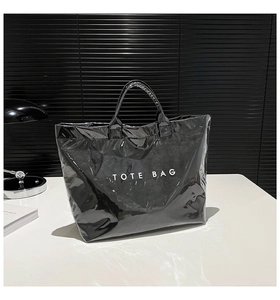 Close-up of black glossy patent leather tote bag with white TOTE BAG lettering detail
