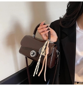 Détail du sac à main en cuir verni marron avec boucle rotative et ruban à carreaux