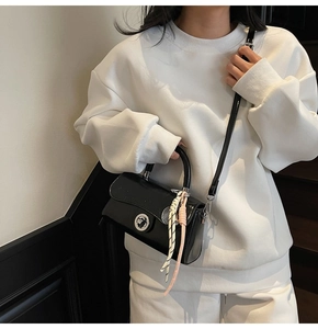 Vue détaillée du sac bandoulière en cuir verni noir avec boucle argentée et pendentif