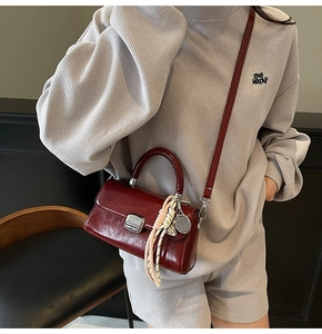 Deep red patent leather crossbody bag with silver lock and decorative charms on a model