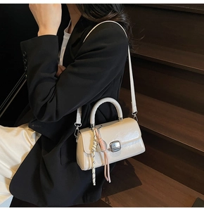 Cream leather handbag featuring a silver twist lock and braided charm detail on black suit