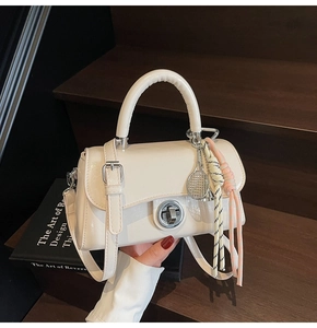 Détail du petit sac en cuir verni crème avec fermoir en métal et breloque raquette