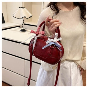 Detail of burgundy glossy leather handbag featuring decorative bows and lace trim on handle