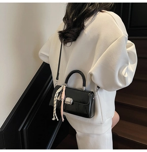 Close-up of black glossy leather handbag with square metal lock and woven charm detail