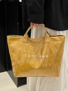 Modern mustard yellow PVC tote bag with glossy wax texture and large white TOTE BAG lettering