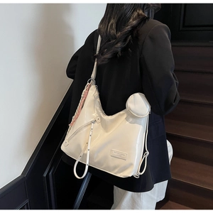 Detail view of large cream patent leather tote bag with side zippers and charm on model