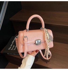 Pink faux leather crossbody bag with silver buckle and braided charm on a wooden step