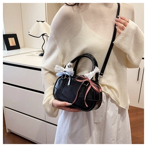 Close-up of black leather Boston bag featuring white lace trim and plaid bow detail