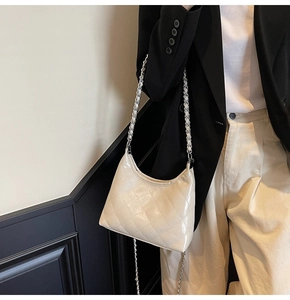 Schicke gesteppte beige Hobo-Tasche mit Silberkette getragen über schwarzem Blazer