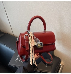 Detail of a dark red handbag with a metal tennis racket charm and woven rope pendants