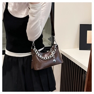 Detailed view of dark brown oil-wax leather bag featuring bold silver chain and pendant