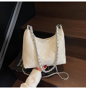 Detailansicht der cremefarbenen Stepptasche mit silberner Kette auf einer Holztreppe