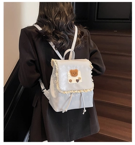 Detailed back view of a light gray backpack with lace trim and bear embroidery on a staircase