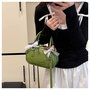 Close-up of avocado green patent leather handbag with lace bows and detachable strap