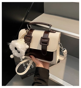 Detail of cream and brown satchel bag with silver buckles and a white plush charm
