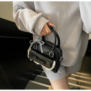 Detail of black glossy bowling bag with lace trim, bow, and patterned ribbon handle