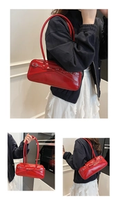Detail of red glossy patent leather underarm bag with bow decoration and silver rivets