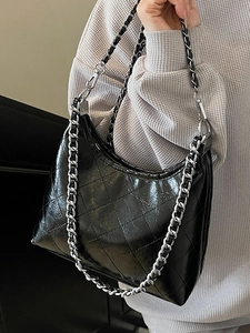 Schwarze gesteppte Halbmondtasche mit silberner Kette über einem grauen Pullover