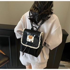 Detail of a black glossy PU backpack featuring lace trim and a brown plush bear patch