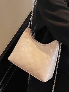 Schicke beige Stepptasche mit silberner Kette, getragen über einem dunklen Sakko