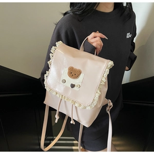 Close-up of pink leather backpack featuring white lace trim and cute plush bear patch decoration