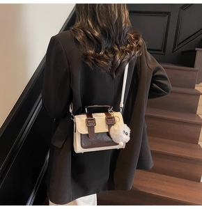 British style satchel bag in beige and dark brown leather worn with a casual black suit