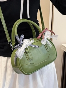 Green leather Boston bag with lace bows and adjustable strap worn by model in home setting