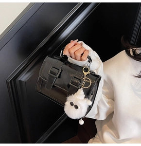 Detail of glossy black leather briefcase bag with buckle straps and plush monster charm