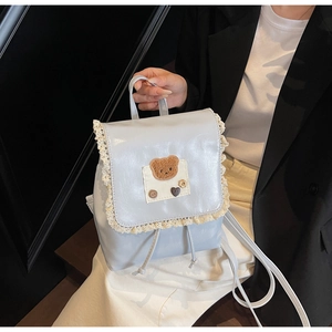Close-up of light blue metallic backpack featuring lace trim and cute plush bear embroidery