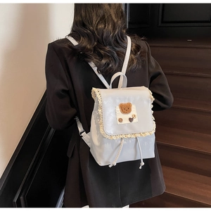 Detail of grey PU leather backpack featuring lace trim, bear patch and drawstring closure