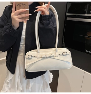 Detail of a creamy white baguette bag with bow decoration and metallic buckle straps