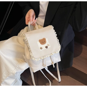 Detail of cream mini backpack featuring teddy bear embroidery and white lace trim edge