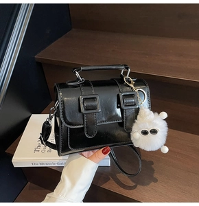 Detail of glossy black Cambridge bag with dual buckle straps and a cute fur pompom