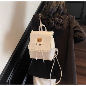 Detail of cream backpack featuring lace trim and a cute teddy bear patch with wooden button