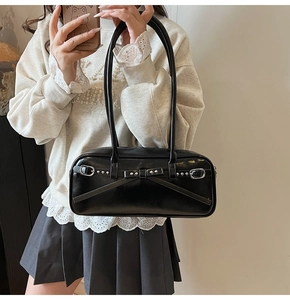 Close-up of black glossy leather shoulder bag with bow straps and silver rivets detail