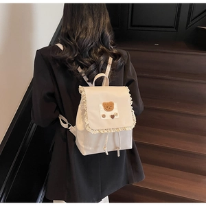 Detail of a creamy white backpack with lace trim and cute bear patch for casual style