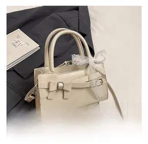 Dettaglio borsa in pelle crema con decorazione a fiocco e nastro in pizzo sul manico
